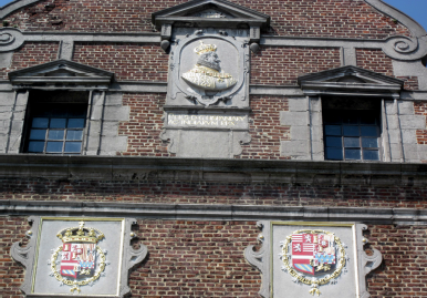 La salle Saint-Georges sur la Grand-Place de Mons. En haut, la représentation en buste de Philippe III d’Espagne. En bas à gauche, les armoiries de Philippe II surmontées de la couronne royale et en bas à droite, les armoiries de Philippe III, toutes deux entourées du collier de la Toison d’Or © IPW